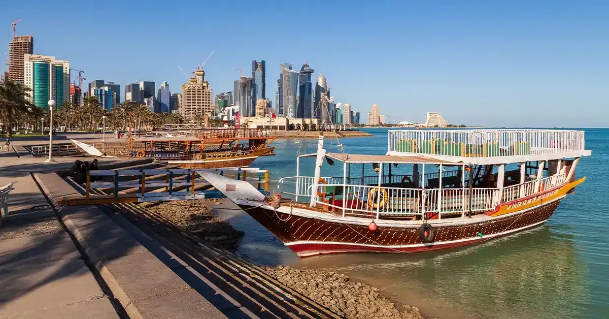 Vibrant cityscape with modern skyscrapers and traditional boat along Doha’s waterfront.