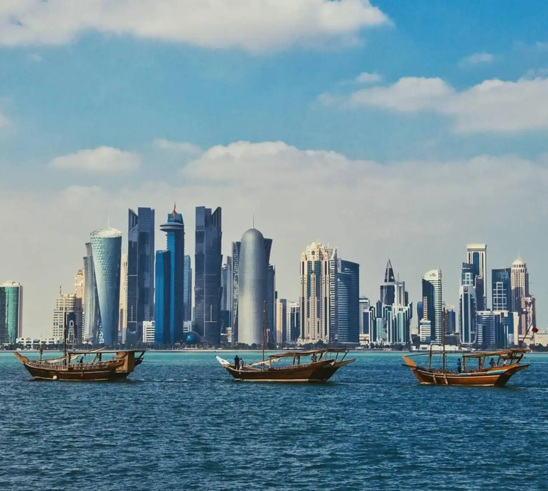 Modern Doha skyline with traditional wooden boats on the water.